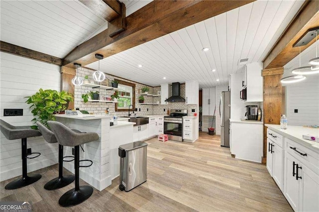 kitchen with appliances with stainless steel finishes, wall chimney range hood, light wood finished floors, a sink, and open shelves