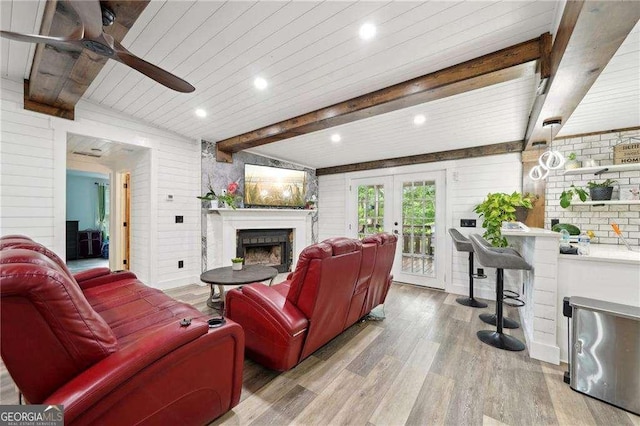 living room with a fireplace, wood finished floors, a ceiling fan, beam ceiling, and french doors