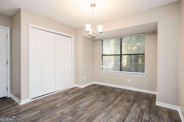unfurnished bedroom featuring wood finished floors, a closet, baseboards, and a chandelier