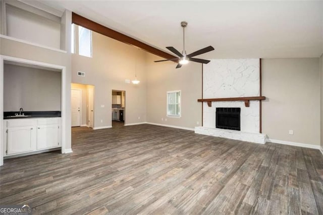 unfurnished living room with ceiling fan, a sink, wood finished floors, a stone fireplace, and high vaulted ceiling