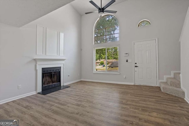 5383 Biffle Way, Stone Mountain, GA 30088 - unfurnished living room featuring ceiling fan, high vaulted ceiling, a fireplace with raised hearth, wood finished floors, and stairs
