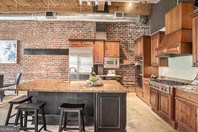 204 Walker St SW Unit 319, Atlanta, GA 30313 - kitchen featuring built in appliances, brick wall, premium range hood, a sink, and light stone counters
