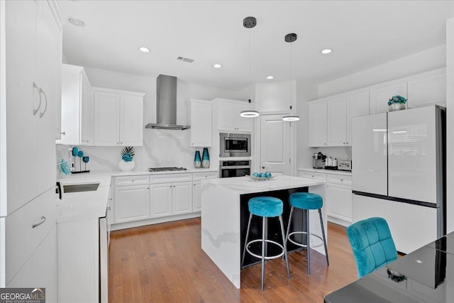 138 Lakestone Pkwy, Woodstock, GA 30188 - kitchen featuring appliances with stainless steel finishes, wall chimney range hood, wood finished floors, a center island, and white cabinetry