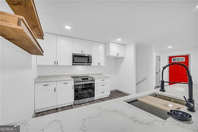 kitchen with stainless steel appliances, a sink, light stone countertops, white cabinets, and wood finished floors