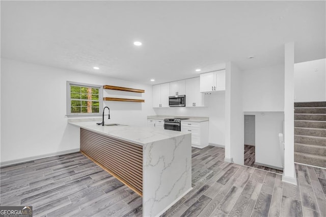 kitchen with appliances with stainless steel finishes, a sink, open shelves, a peninsula, and light wood finished floors