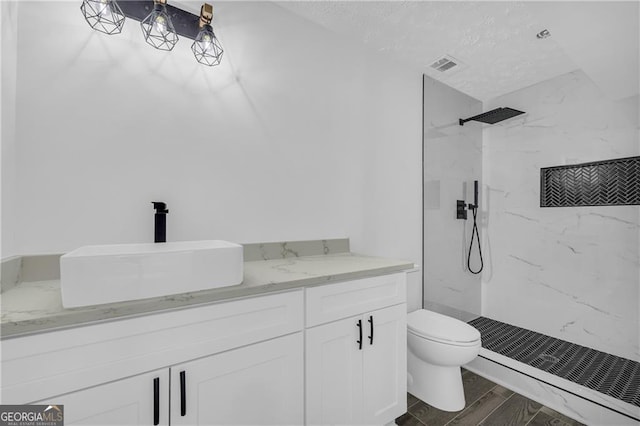 bathroom with a marble finish shower, toilet, vanity, wood finished floors, and a textured ceiling