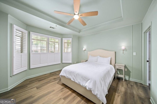 bedroom featuring a tray ceiling, crown molding, wood finished floors, a ceiling fan, and baseboards