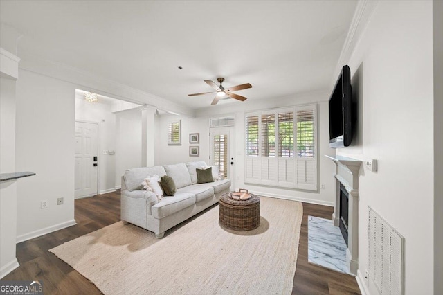 living room with ornamental molding, ceiling fan, dark wood-style flooring, a fireplace with flush hearth, and baseboards