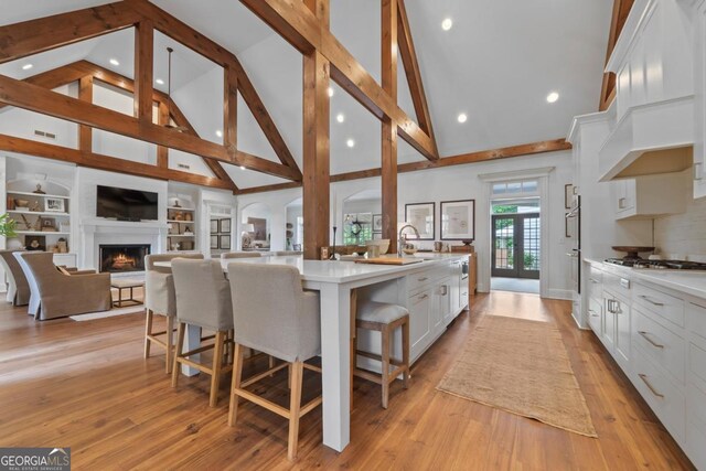 143 Wildwood Dr, Eatonton, GA 31024 - kitchen featuring high vaulted ceiling, white cabinetry, light countertops, a warm lit fireplace, and a large island with sink