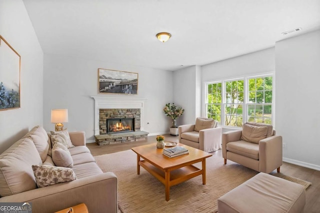 living room featuring wood finished floors, a stone fireplace, and baseboards