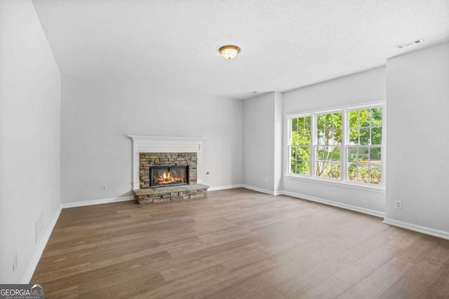 unfurnished living room featuring wood finished floors, baseboards, a stone fireplace, and a textured ceiling