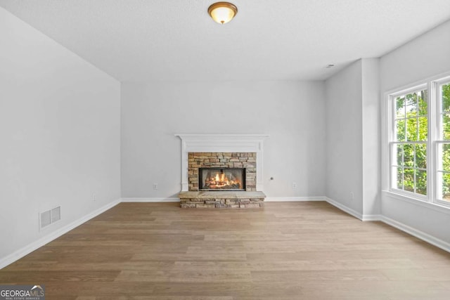 unfurnished living room with healthy amount of natural light, wood finished floors, baseboards, and a stone fireplace