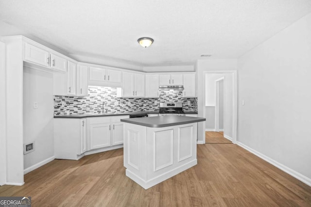 kitchen featuring stainless steel electric range, dark countertops, a sink, decorative backsplash, and white cabinets