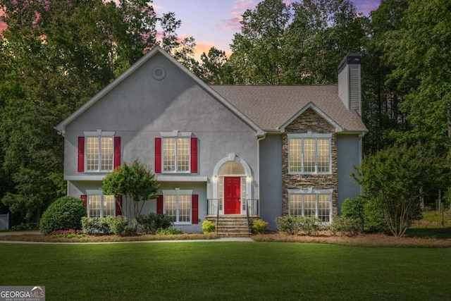 raised ranch featuring stone siding, a yard, a chimney, and stucco siding