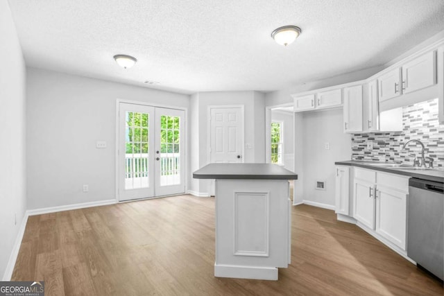 kitchen featuring a sink, dishwasher, wood finished floors, dark countertops, and a textured ceiling
