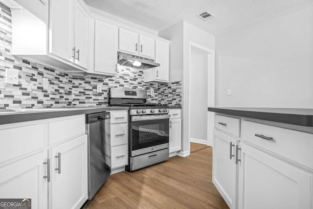 kitchen with stainless steel appliances, under cabinet range hood, dark countertops, white cabinets, and decorative backsplash