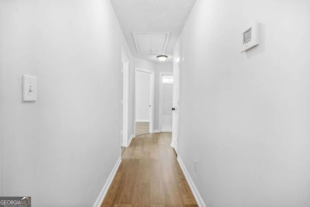 hall featuring attic access, wood finished floors, baseboards, and a textured ceiling