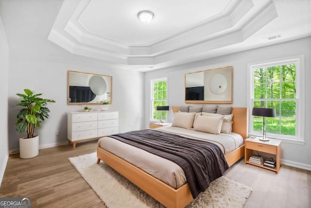 bedroom with a raised ceiling, ornamental molding, wood finished floors, and baseboards