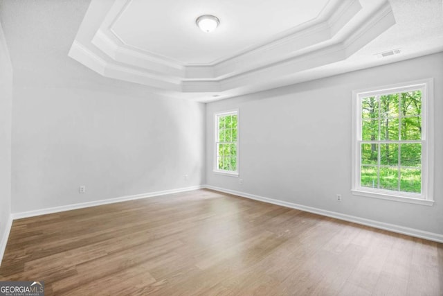 unfurnished room featuring a tray ceiling, ornamental molding, wood finished floors, and baseboards