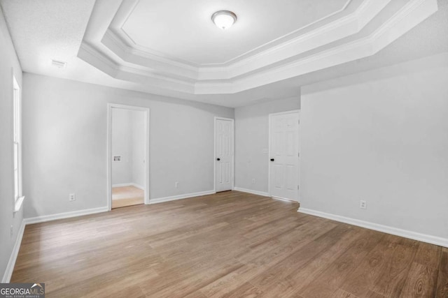 unfurnished room featuring a tray ceiling, light wood-style flooring, crown molding, and baseboards