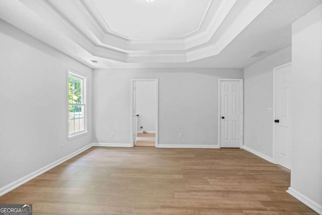 unfurnished room with a tray ceiling, light wood-style floors, ornamental molding, and baseboards