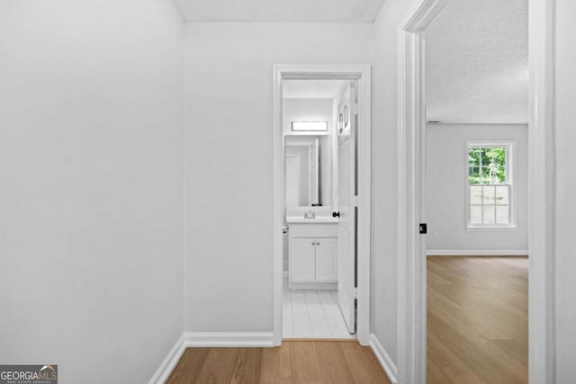 hallway featuring a sink, wood finished floors, baseboards, and a textured ceiling