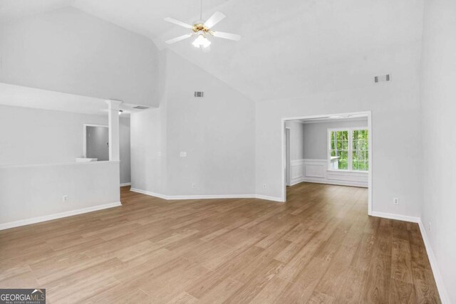 unfurnished living room with high vaulted ceiling, ceiling fan, ornate columns, light wood-style flooring, and baseboards