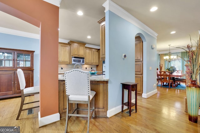 kitchen featuring stainless steel microwave, a breakfast bar area, crown molding, arched walkways, and baseboards