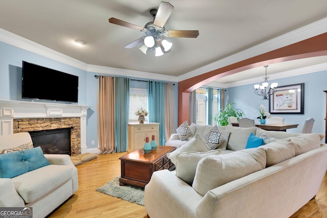 living area featuring crown molding, arched walkways, a chandelier, a stone fireplace, and light wood-style flooring