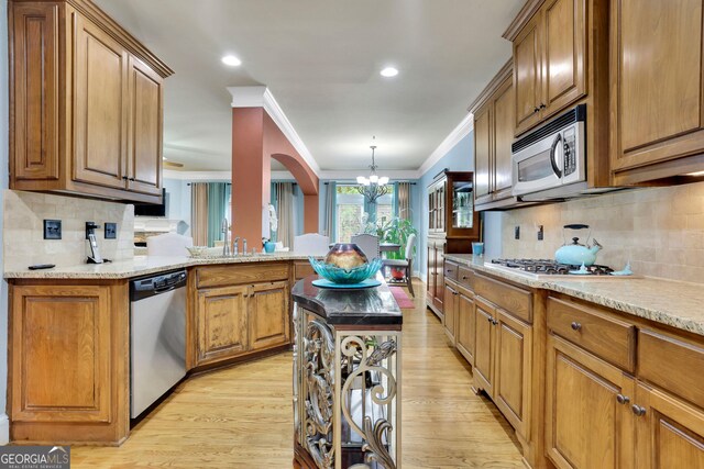 kitchen featuring stainless steel appliances, a chandelier, brown cabinets, light wood-style flooring, and ornamental molding