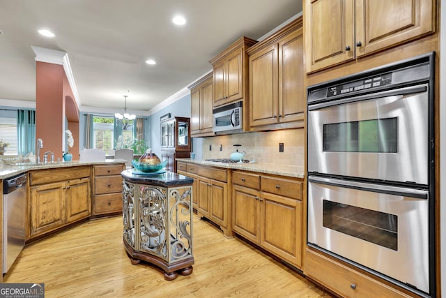 kitchen featuring appliances with stainless steel finishes, a chandelier, ornamental molding, a sink, and light wood-style floors