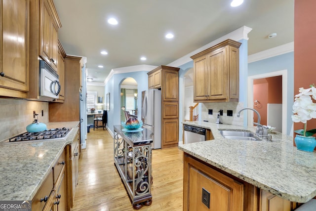 kitchen with a sink, appliances with stainless steel finishes, crown molding, light wood-style flooring, and light stone counters