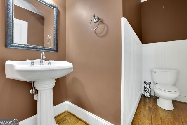 half bath featuring wood finished floors, toilet, and wainscoting