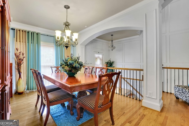 dining space featuring a chandelier, arched walkways, healthy amount of natural light, crown molding, and a decorative wall