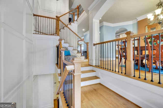 staircase with crown molding, a decorative wall, a chandelier, wood finished floors, and a towering ceiling