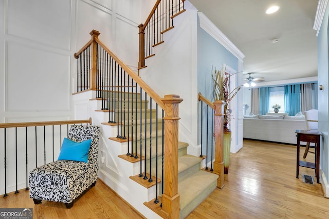 stairway with wood finished floors, crown molding, and ceiling fan