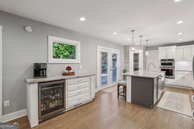 kitchen with beverage cooler, double oven, white cabinets, recessed lighting, and light stone countertops