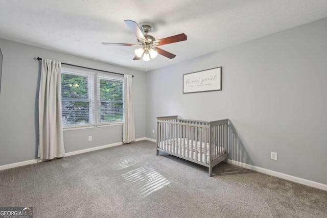carpeted bedroom featuring a nursery area, baseboards, and ceiling fan