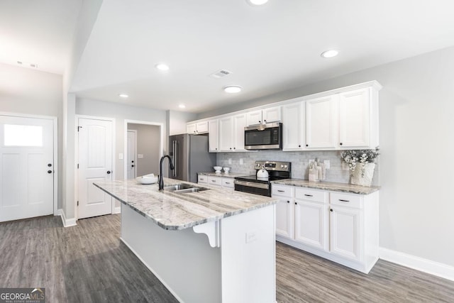 kitchen with stainless steel appliances, a kitchen island with sink, white cabinets, tasteful backsplash, and wood finished floors