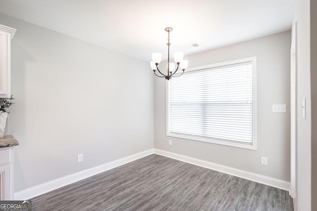 spare room featuring a chandelier, dark wood finished floors, and baseboards