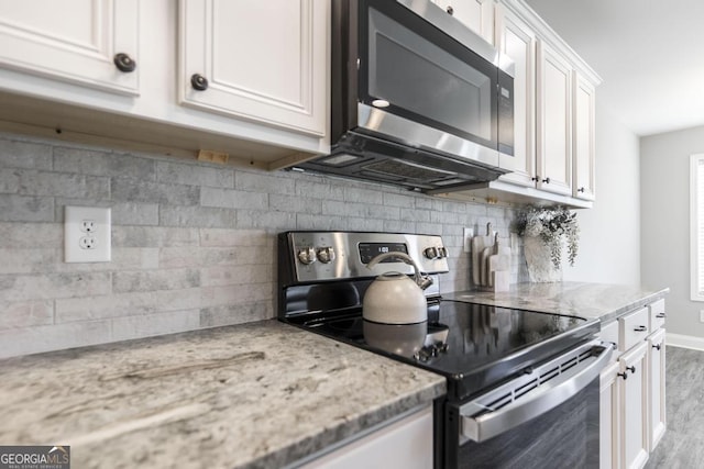 kitchen with appliances with stainless steel finishes, wood finished floors, white cabinetry, and light stone countertops