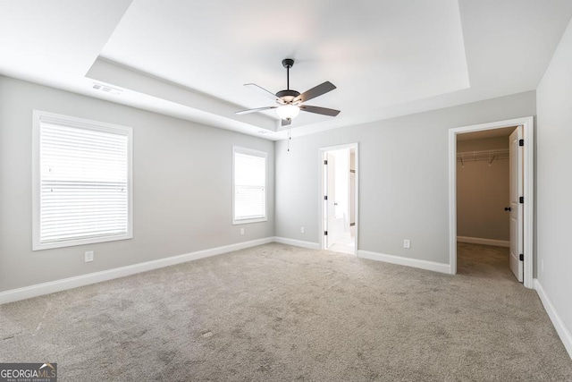 unfurnished bedroom with a raised ceiling, a spacious closet, carpet, and baseboards