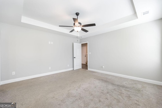 carpeted empty room with a raised ceiling, baseboards, and ceiling fan
