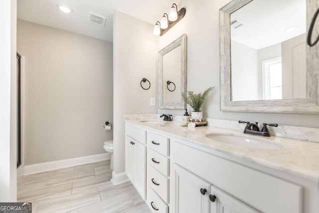 bathroom featuring toilet, baseboards, and double vanity