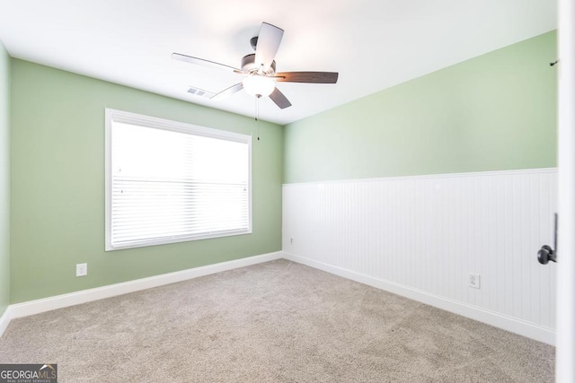 carpeted empty room featuring ceiling fan and wainscoting