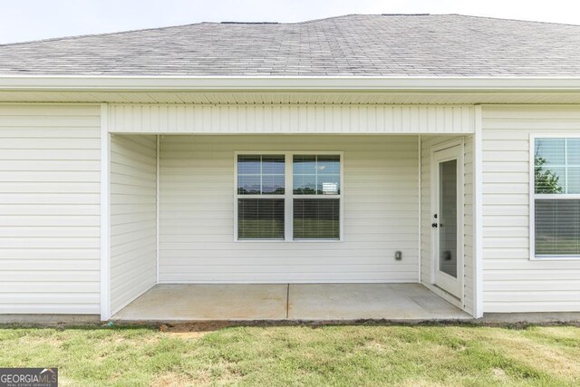property entrance with roof with shingles, a patio, and a lawn