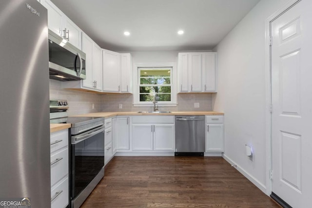 kitchen featuring stainless steel appliances, a sink, tasteful backsplash, dark wood finished floors, and white cabinetry
