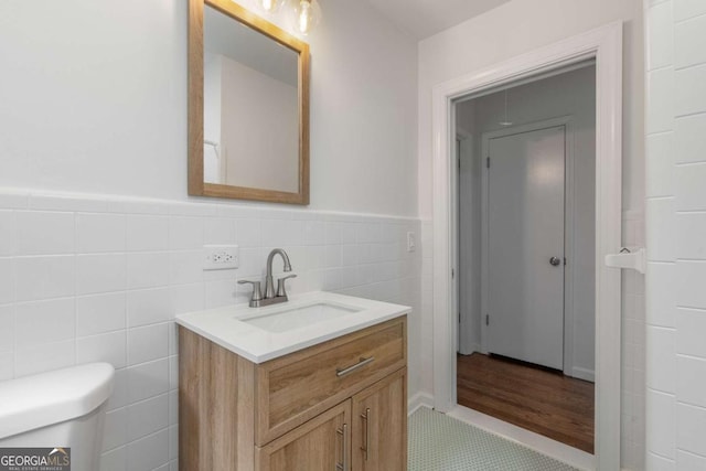bathroom featuring vanity, toilet, a wainscoted wall, tile walls, and tile patterned flooring