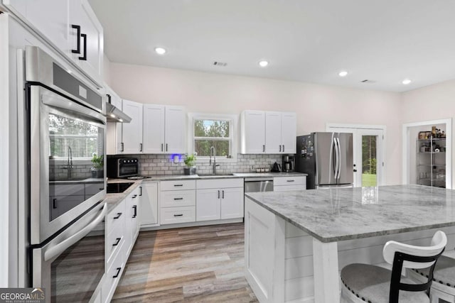 kitchen featuring appliances with stainless steel finishes, a breakfast bar, a sink, light wood finished floors, and backsplash
