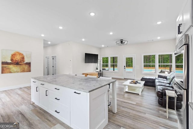kitchen featuring open floor plan, stainless steel double oven, a center island, light stone countertops, and light wood finished floors
